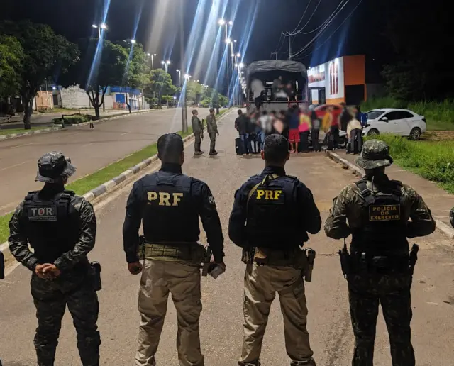 Policiais veem grupo de imigrantes sendo colocados em caminhão para transporte 