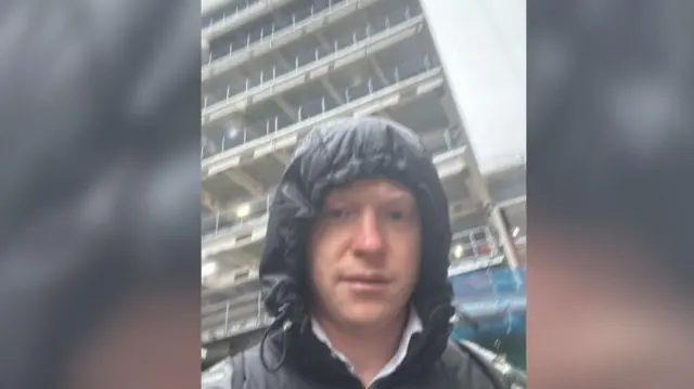 Sol com capuz na chuva em frente a um prédio alto.