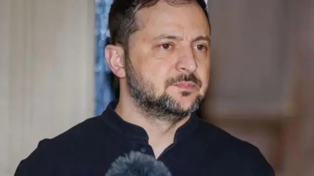 Perezida wa Ukraine Volodymyr Zelensky ahagaze, imbere ye haboneka igice cy'indangururamajwi