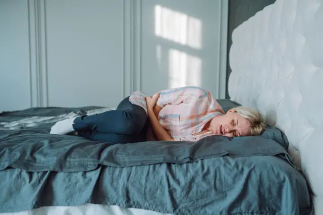 Yatakta uzanan ve karnını tutan bir kadın fotoğrafı. 