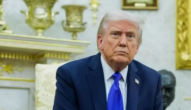 Трамп у темному діловому костюмі і синій краватці сидить у кабінеті 