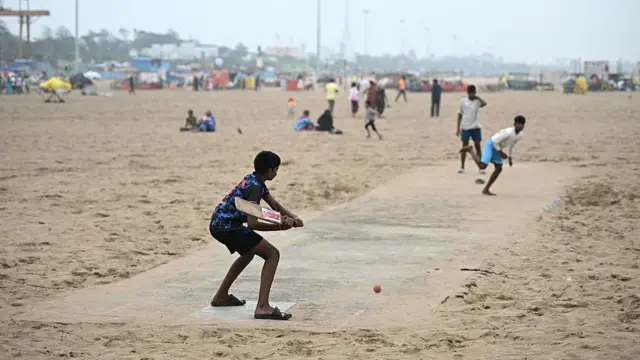 Children play cricket on a beach in India - a batter prepares take a swing at a ball delivered on a rudimentary track.