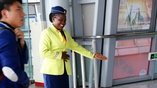 mtumishi msichana wa treni akiwaashiria abiria mahala pa kuabiria.