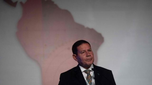 Hamilton Mourãobet aposta para presidentepé, falando, com painel expondo mapa do Brasil atrás