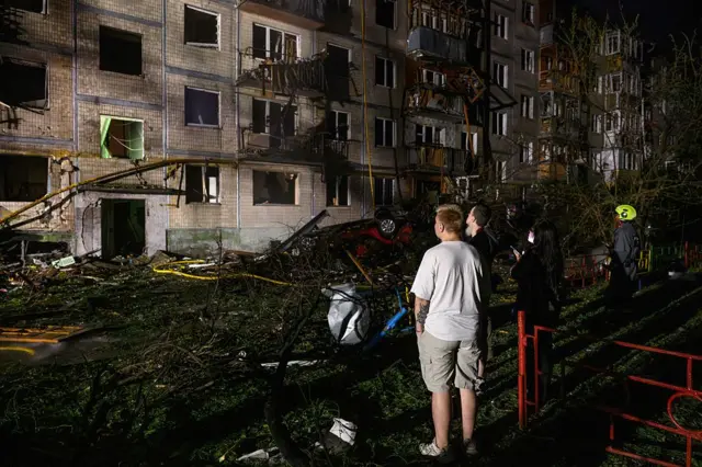 Мужчины стоят ночью у разрушенной пятиэтажки в Киеве