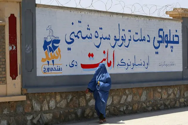 امرأة أفغانية ترتدي البرقع تمر بجانب جدارية تحيي الذكرى الخامسة لعودة حركة طالبان إلى السلطة، في ولاية غزني الأفغانية، في 13 أغسطس/آب 2026.