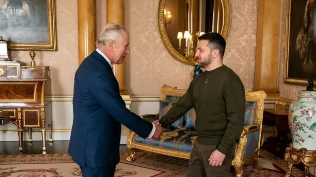Король Чарльз III та Володимир Зеленський тиснуть руки в середині розкішної кімнати з золотими оздобленнями
