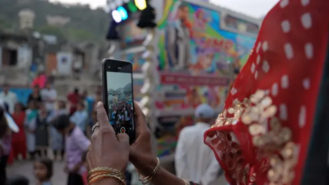 घूंघट के पीछे से देखते हुए औरत मोबाइल फोन से वीडियो बना रही है.