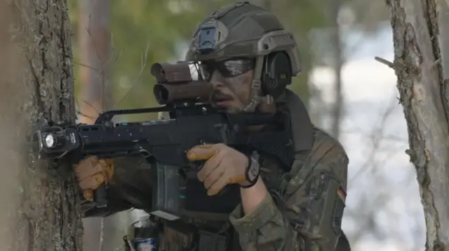 Um soldado com um fuzil, vestindo uniforme camuflado