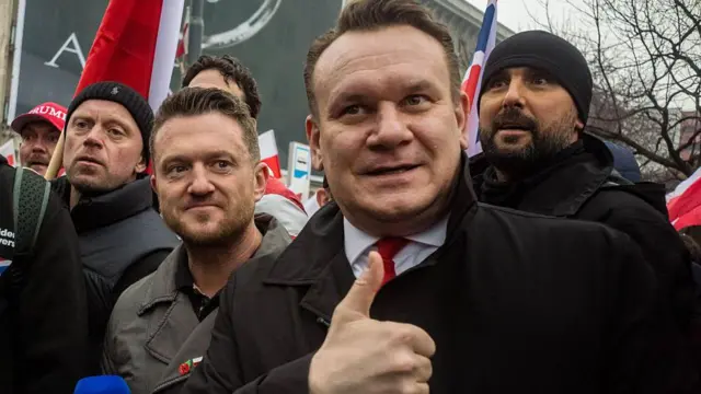 Polski poseł do Parlamentu Europejskiego Dominik Tarczyński na zdjęciu pokazuje kciuk w górę. Tommy Robinson jest po jego lewej stronie, obserwując demonstrację.