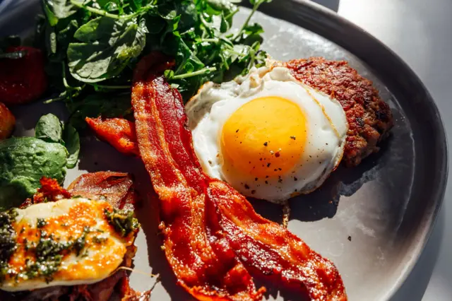 Un plato con carne, huevo, tocino y espinaca, todos alimentos con proteína.