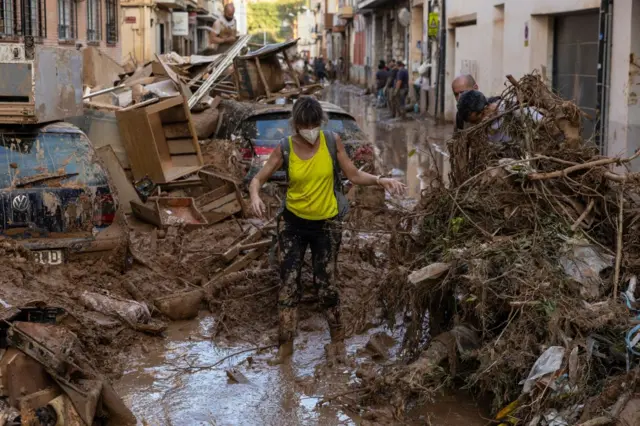 A woman walks along a street full of mud and waste from houses after heavy rain and flooding