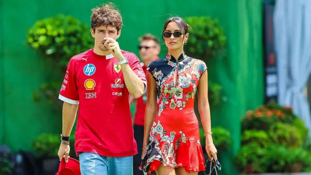 Charles Leclerc z Ferrari, ubrany w czerwoną koszulkę idzie ze swoją dziewczyną, Alexandrą Saint Mleux, ubraną w czerwoną sukienkę z kolorowymi kwiatami, podczas Grand Prix Formuły 1 Singapuru 