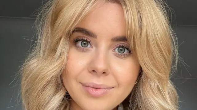 Sammi Claxon, fotografada olhando diretamente para a câmera. Ela tem cabelos loiros e olhos verdes