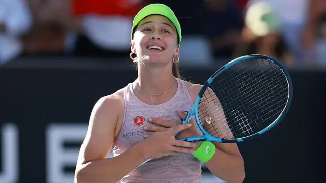 Zeynep Sönmez elini göğsüne koymuş, seyircilere büyük bir sevinç içinde bakıyor. Kafasında yeşil siperli bir şapka var