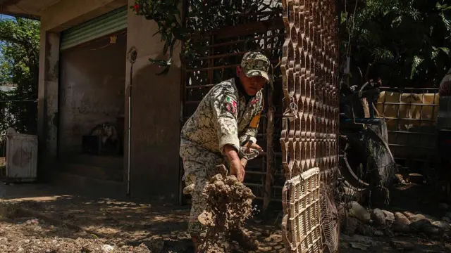 Un soldado vestido en fatigas usa una pala para despejar el lodo frente a una casa