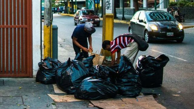 Dos hombres buscan comida en la basura en Caracas.