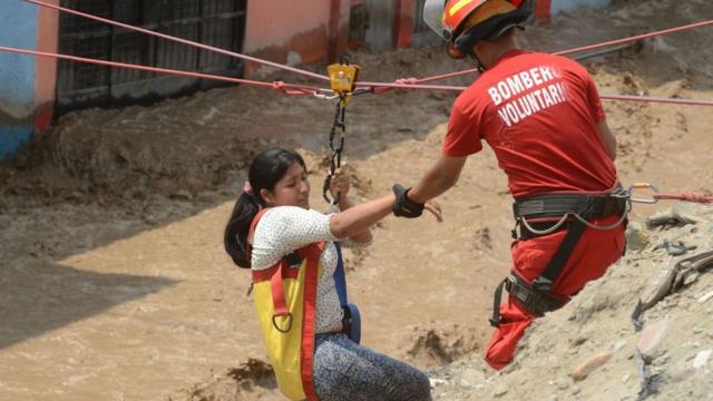 Bombero rescatando a una pobladora de Huachipa para que no se la lleve la corriente de un huaico.