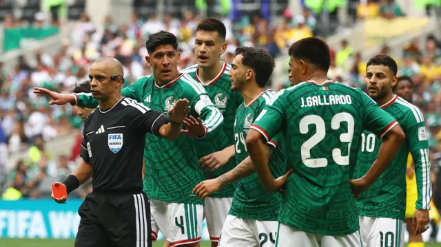 رد فعل المكسيكي سيزار مونتيس بعد حصوله على بطاقة حمراء من الحكم ويلتون سامبايو بينما احتج المكسيكيان إدسون ألفاريز ولويس تشافيز. يرتدي لاعبو الفريق المكسيكي قمصاناً خضراء اللون وبناطيل قصيرة بلون أبيض، يقف عدد منهم وراء الحكم الذي يرتدي زياً رياضياً أسود اللون ومخططاً بثلاث خطوط بيضاء من الجانب.