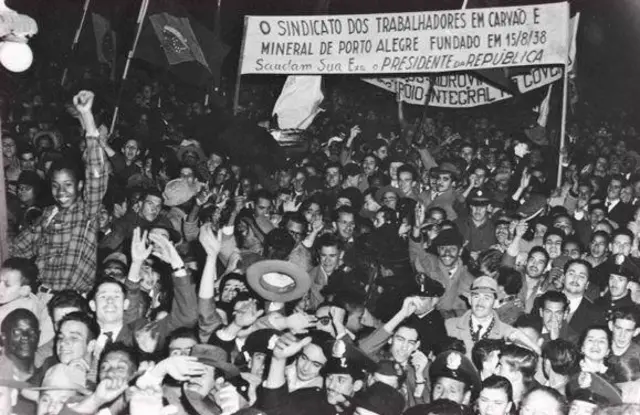 Pessoas aglomeradas com cartazes em foto em preto e branco