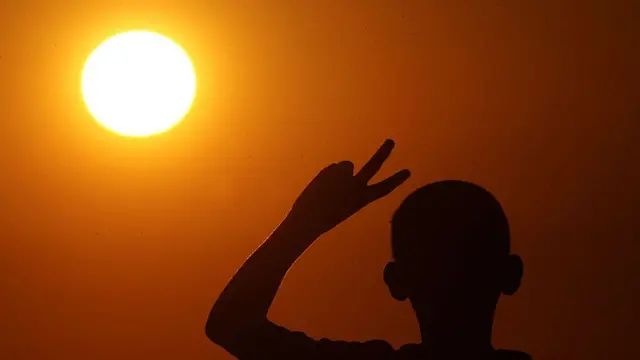Imagen de un atardecer naranja intenso y la silueta de un niño.
