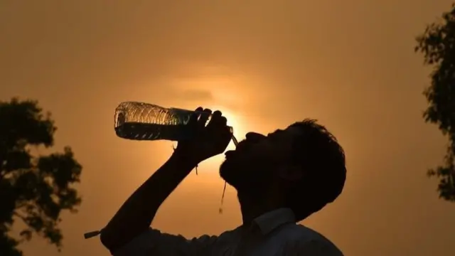 Um homem bebe águasportsbet io bonusuma garrafa com o sol ao fundo