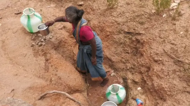 குழிக்குள் இருந்து தண்ணீர் எடுக்கும் மூதாட்டி