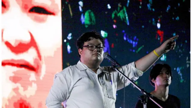 เพนกวิน-พริษฐ์ ชิวารักษ์ นักศึกษาคณะรัฐศาสตร์ มธ. ประกาศเชิญชวนผู้ชุมนมให้แสดงออกเชิงสัญลักษณ์ 8 ข้อ อาทิ ชูสามนิ้วขณะเคารพธงชาติ, บีบแตรในขบวนรถบุคคลสำคัญ, ถอนเงินฝากจากธนาคารไทยพาณิชย์