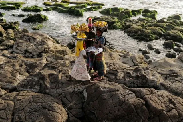 Girls stand on the rocks looking at a magazine.