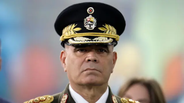 Padrino é um homem branco, sem barba, de meia idade, vestindo farda e uma boina militar.