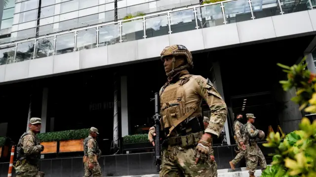 Fotos of heavily armed members of di National Aeronaval Service of Panama dey wear masks and guard di hotel wia di deported migrants dey stay