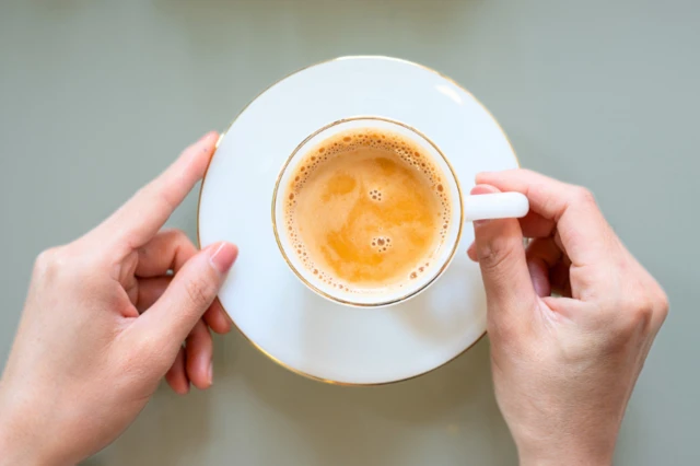A woman's hand holding a cup of Masala tea on table