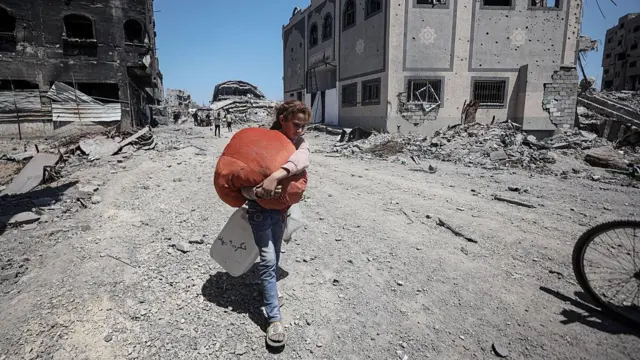 Bir genç Filisitinli kız elinde büyük bir bohçayla yıkıntılar arasında ilerliyor.