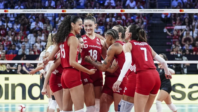 Türkiye formalı voleybolcular file önünde toplu halde sevinç yaşıyor. Arkada dolu tribünler görünüyor.