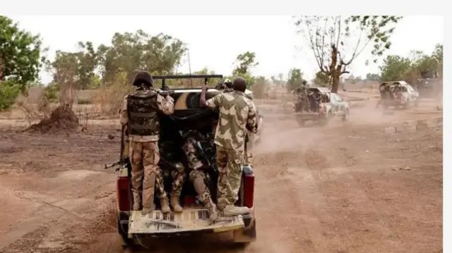 Aworan yii ṣafihan ikọ to wọsọ ologun ninu ọkọ, awọn kan jokoo, awọn kan si duro, ọkọ ologun meji miran n lọ niwaju wọn