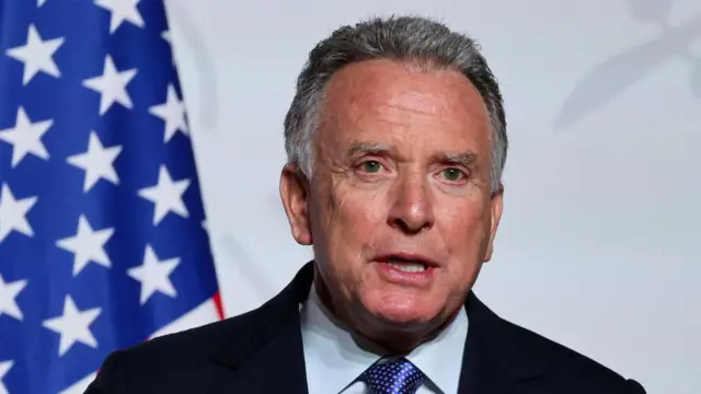 An image of the US Special Envoy to the Middle East, Steve Witkoff, speaking in front of the American Flag visible to the left.