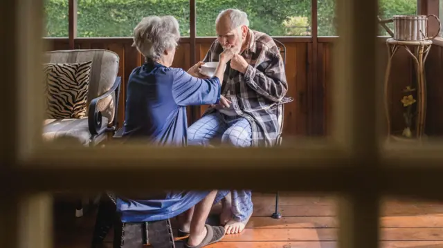 Una cuidadora alimenta a un anciano