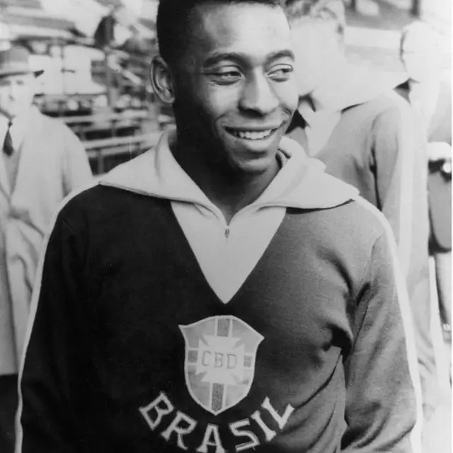 Em foto preto e branco, Pelé sorri, com casaco do Brasil