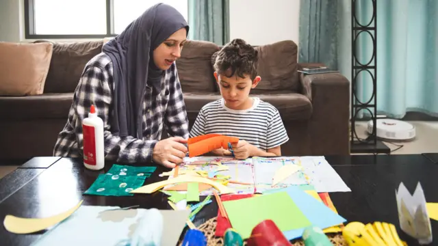 أم وطفلها يصنعان زينة من الورق لشهر رمضان في غرفة المعيشة.