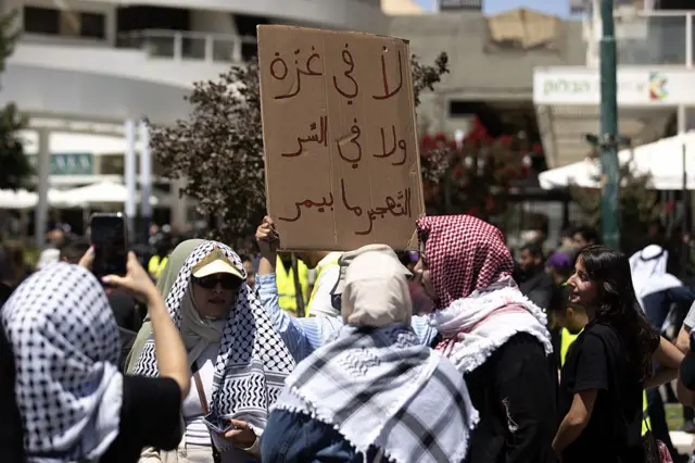 سيدات ورجال يرتدون الكوفية والشماغ ويرفعون لافتة كُتب عليها "لا في غزة ولا في السرّ.. التهجير ما بيمرّ"