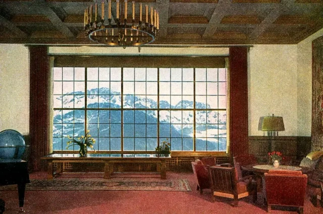 نمایی از اتاقی بزرگ با پنجره بزرگ به کوه‌های برفی، چند مبل و میز در اتاق دیده می‌شود