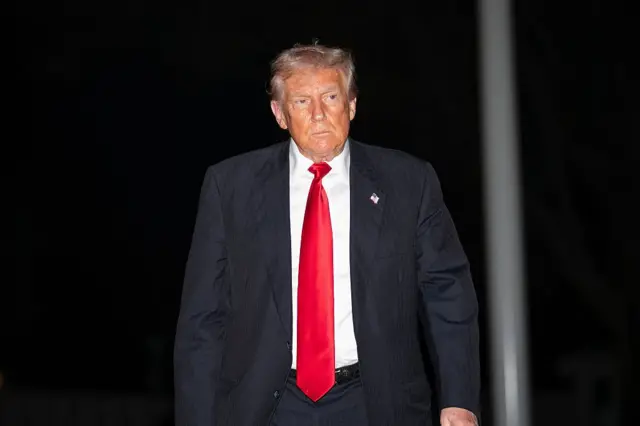 Donald Trump caminhando. Ele usa uma gravata vermelha e terno preto