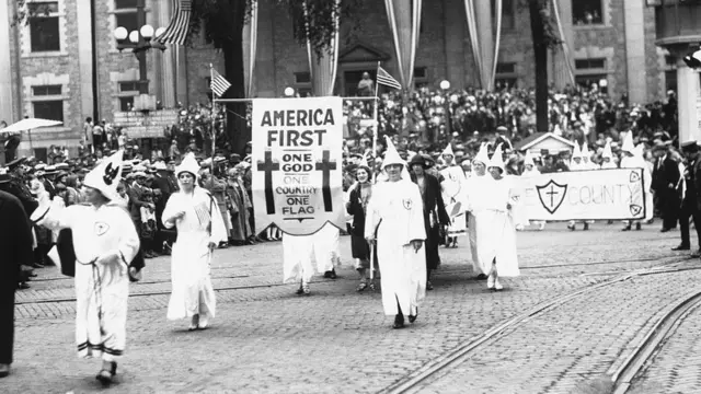 Marcha del Ku Klux Klan con un cartel con "America first" en la década de 1920.