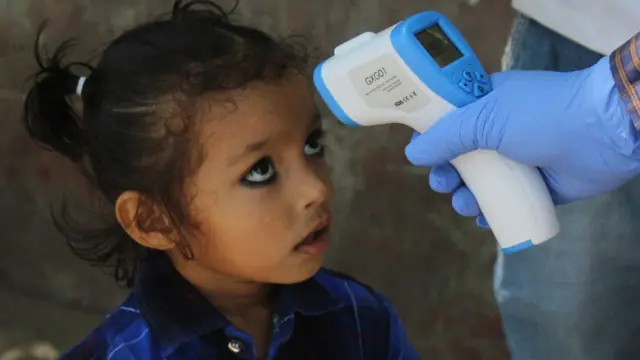 બાળકીનું થર્મલ સ્ક્રિનિક કરી રહેલ આરોગ્ય કર્મચારીની તસવીર