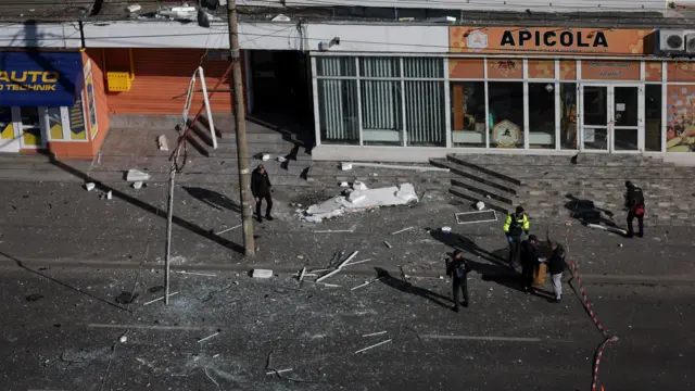 Вид сверху на улицу с обломками, работники расчищают последствия попадания дрона.