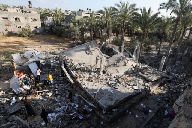 فلسطينيون يتفقدون الأضرار في موقع غارة إسرائيلية على منزل في دير البلح وسط قطاع غزة، 21 مايو/أيار 2025.