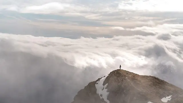 Pessoa sozinha no alto de uma montanha, com nuvens ao fundo