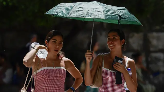 دوې نجونې، چې د اوبو بوتلونه ورسره دي، پر ځانونه یې چترۍ نیولې ده.