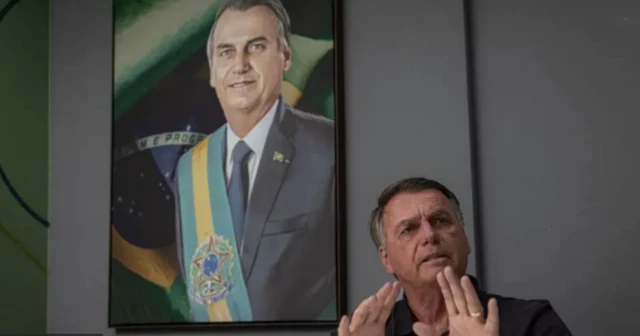 Jair Bolsonaro com as mãos abertas diante de um quadro com uma pintura sua usando a faixa presidencial