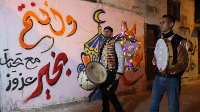 "Musaharatis" di Palestina berjalan melewati grafiti mural sambil menabuh genderang saat mereka berkeliling di Rafah di Jalur Gaza selatan pada malam pertama Ramadan, Kamis (23/03). 